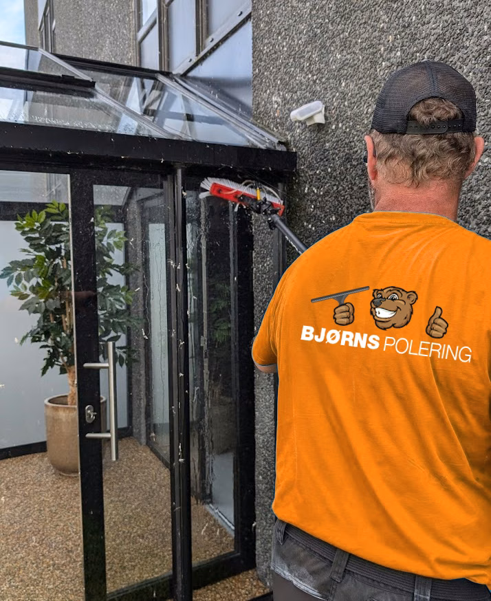 Kim i arbejdstøj med Bjørns Polerings logo pudser et glastag med vaskeanlæg